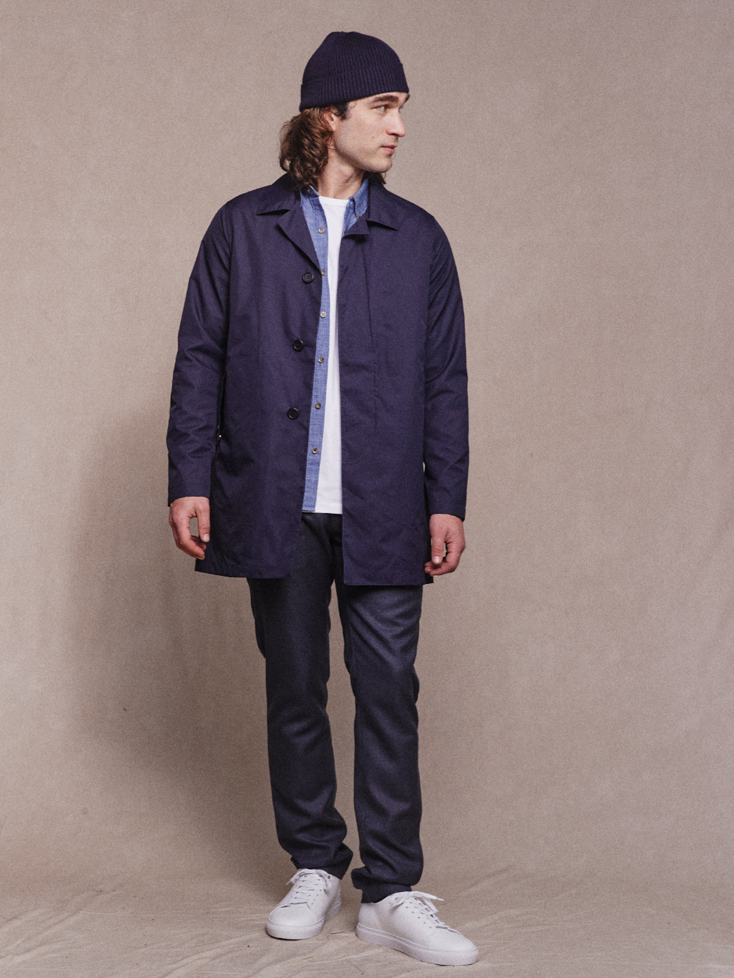 Model wearing Rain Mac Jacket in Navy with Navy Beanie, Denim Shirt, White Tee, Smart Trousers and White Sneakers