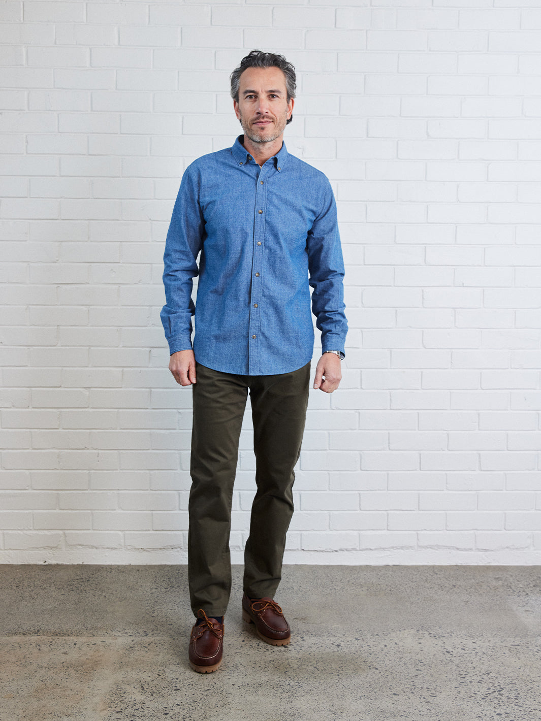 Model wearing denim button down with khaki chinos and brown boat shoes