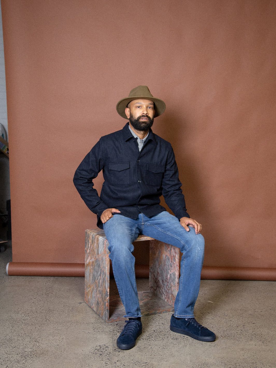 Model sitting down wearing full Asuwere outfit including navy woollen shacket and navy suede leather shoes