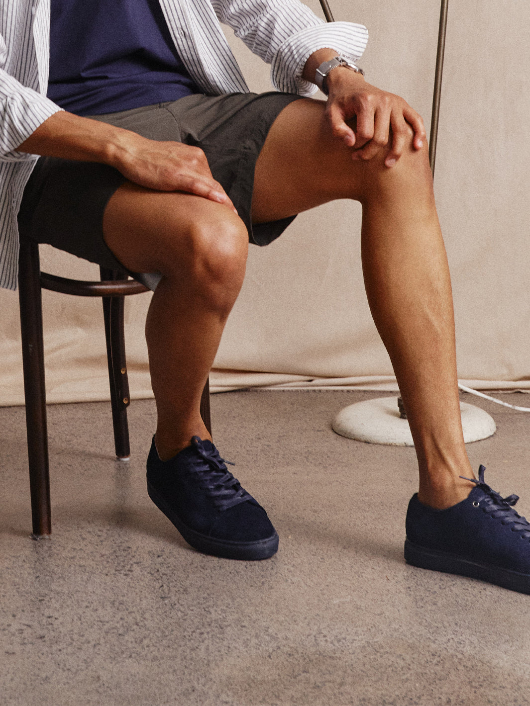Model sitting down wearing Asuwere navy suede leather low sneakers with shorts and striped shirt
