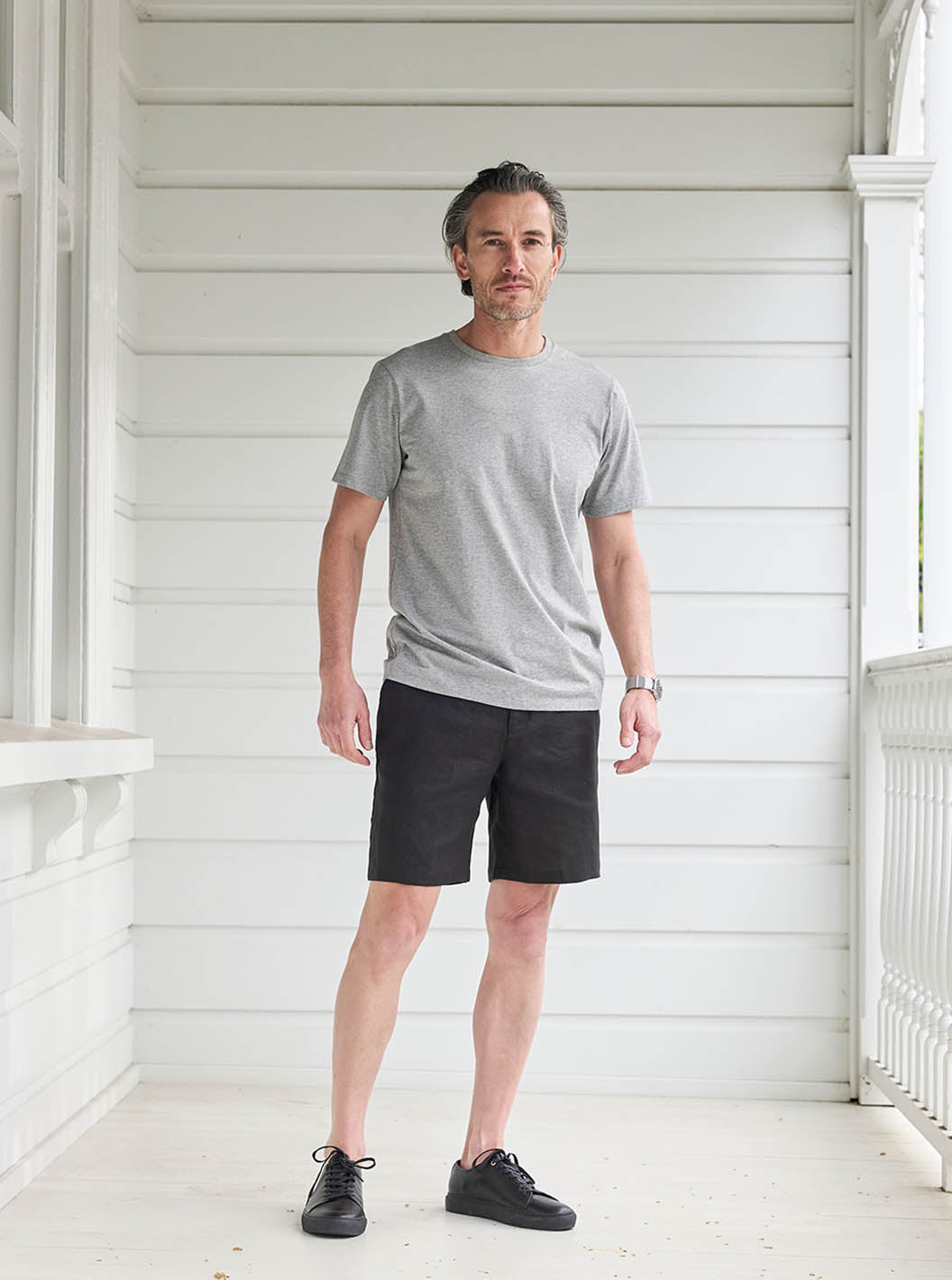 Model standing on white deck wearing Bound Pima Tee in Grey with Black Shorts and Sneakers 