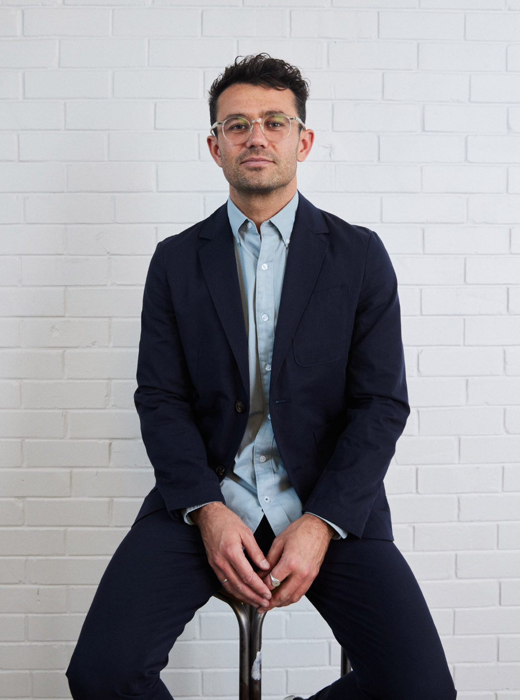 Model sitting down wearing dusty blue poplin button down with navy blazer and chinos
