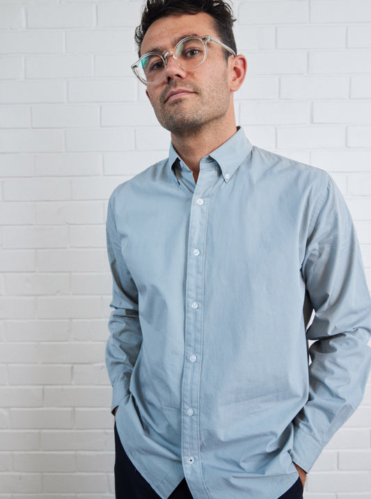 Model with glasses wearing dusty blue poplin button down shirt